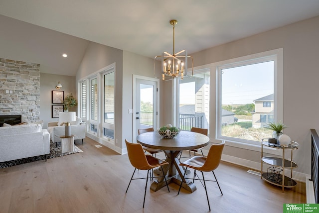 dining area with a fireplace, light hardwood / wood-style floors, an inviting chandelier, and lofted ceiling