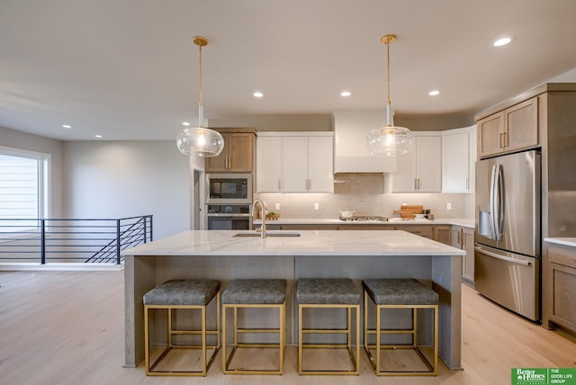 kitchen featuring white cabinets, appliances with stainless steel finishes, a center island with sink, and light stone countertops