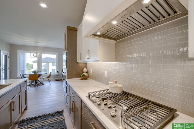 kitchen featuring stainless steel appliances, a notable chandelier, backsplash, pendant lighting, and custom range hood