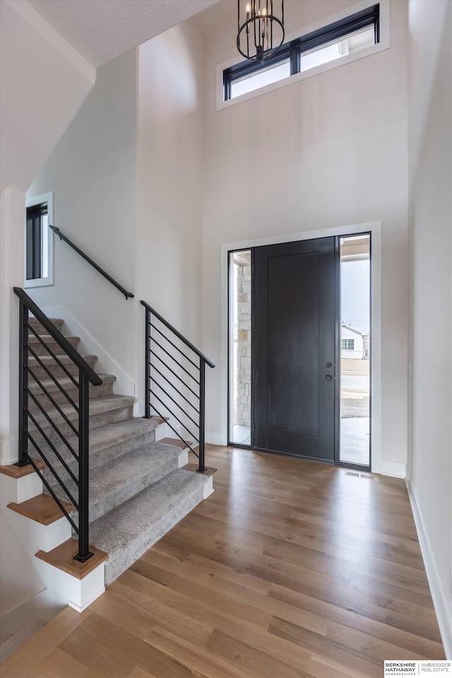 entrance foyer with a towering ceiling, wood-type flooring, and a chandelier