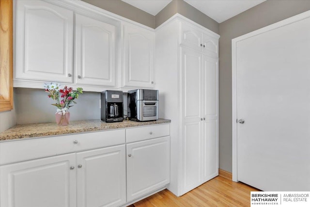 kitchen with light wood-type flooring, white cabinetry, and light stone counters