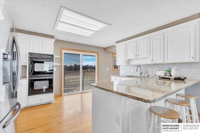 kitchen featuring kitchen peninsula, stainless steel fridge, light stone countertops, double oven, and white cabinetry