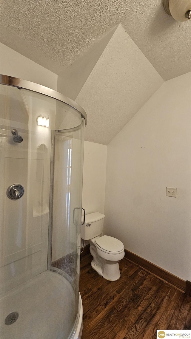 bathroom featuring vaulted ceiling, hardwood / wood-style flooring, toilet, a textured ceiling, and walk in shower