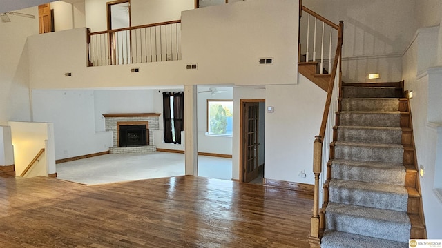 stairs with a fireplace, hardwood / wood-style floors, a towering ceiling, and ceiling fan