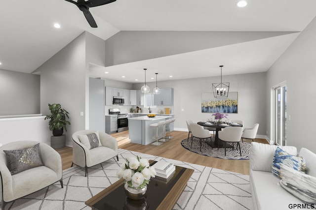 living room with ceiling fan with notable chandelier, light hardwood / wood-style floors, and high vaulted ceiling