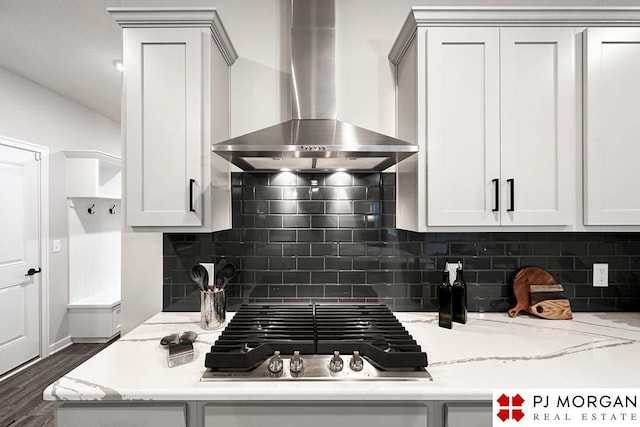 kitchen featuring wall chimney exhaust hood, stainless steel gas cooktop, light stone counters, backsplash, and white cabinets