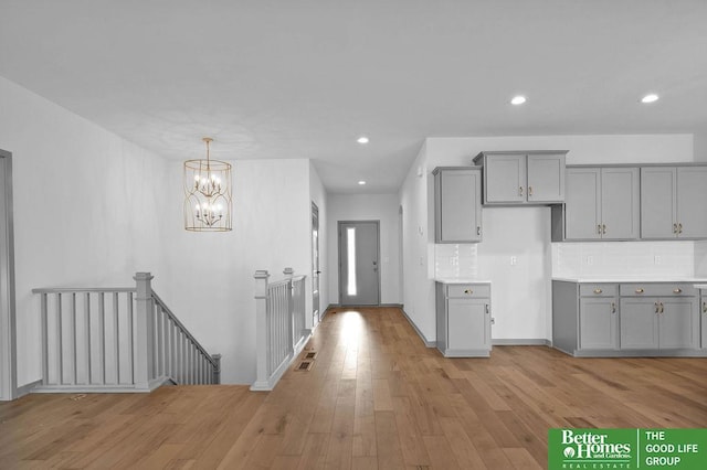 kitchen featuring gray cabinetry, a chandelier, light wood-type flooring, and tasteful backsplash