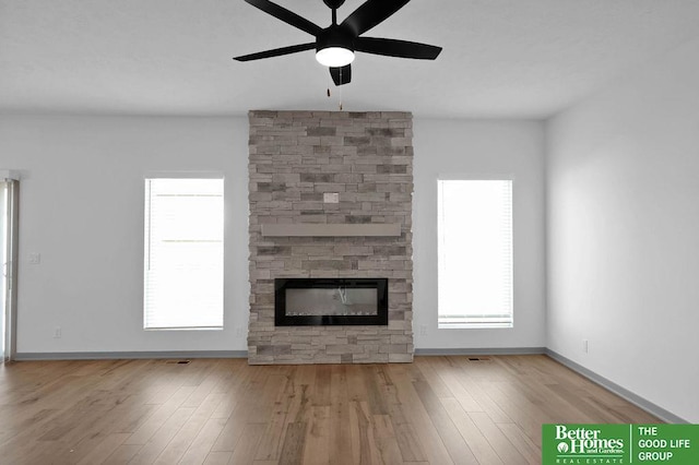 unfurnished living room with a stone fireplace, ceiling fan, and light hardwood / wood-style floors