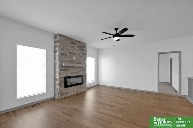 unfurnished living room with a stone fireplace, ceiling fan, and light hardwood / wood-style floors