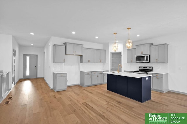 kitchen with gray cabinetry, decorative light fixtures, an island with sink, and appliances with stainless steel finishes