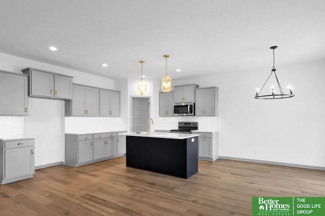 kitchen with gray cabinets, stainless steel appliances, hanging light fixtures, and an island with sink