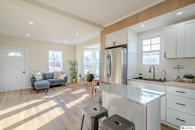 kitchen featuring sink, decorative backsplash, light hardwood / wood-style floors, white cabinetry, and stainless steel refrigerator