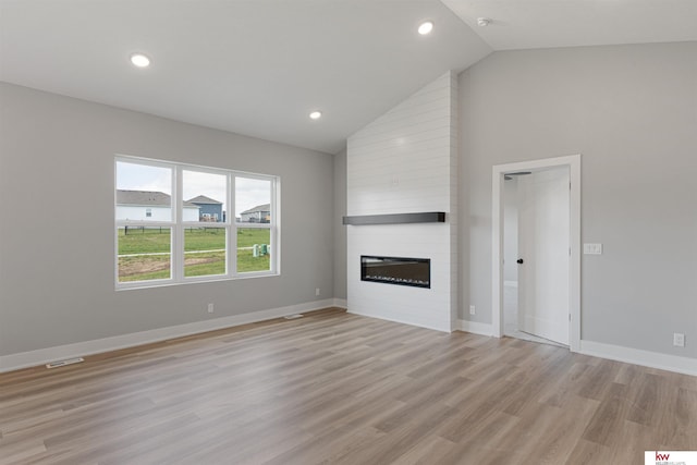 unfurnished living room featuring a large fireplace, light hardwood / wood-style floors, and high vaulted ceiling