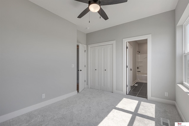 unfurnished bedroom featuring dark carpet, ceiling fan, multiple windows, connected bathroom, and a closet