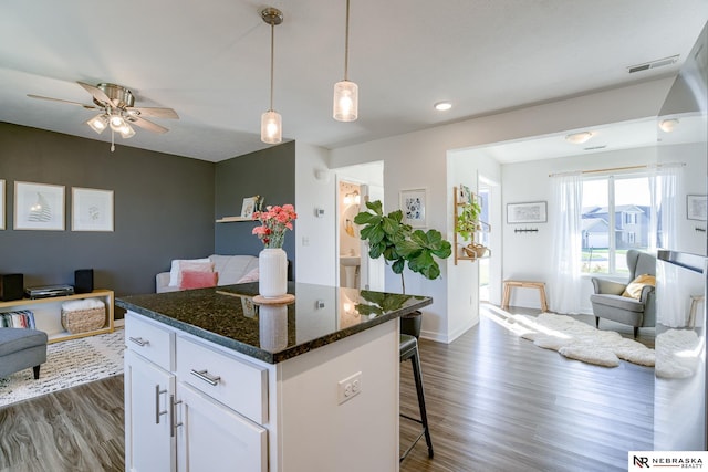 kitchen with white cabinetry, a center island, hanging light fixtures, dark stone counters, and a breakfast bar