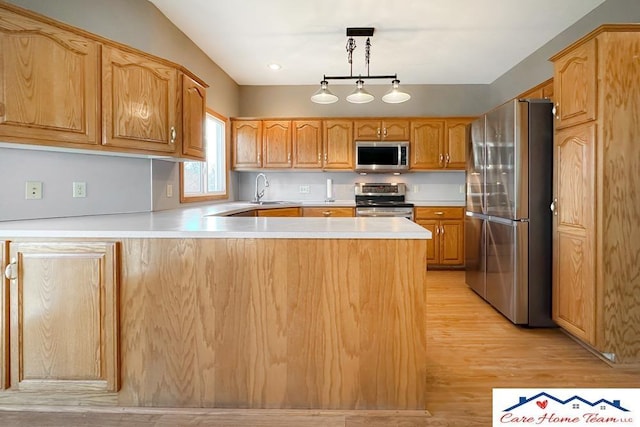 kitchen featuring kitchen peninsula, appliances with stainless steel finishes, sink, light hardwood / wood-style flooring, and hanging light fixtures