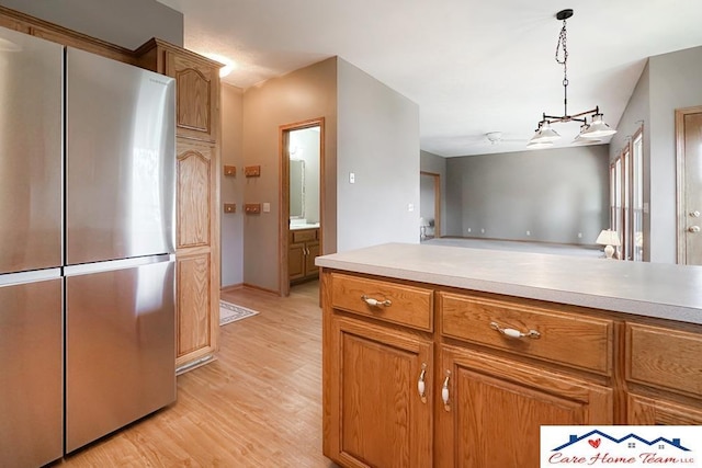 kitchen featuring light wood-type flooring, hanging light fixtures, and stainless steel refrigerator