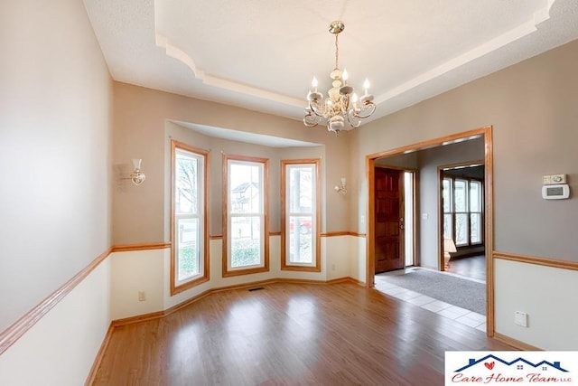 unfurnished room featuring a tray ceiling, an inviting chandelier, and hardwood / wood-style flooring