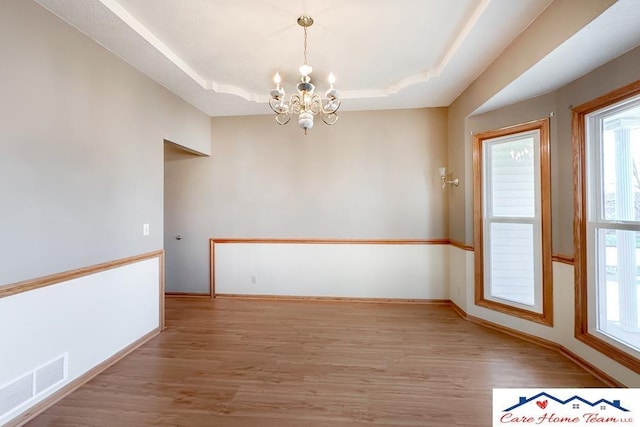 empty room featuring a tray ceiling, a chandelier, and hardwood / wood-style flooring