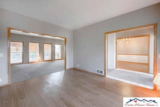 empty room with a notable chandelier and light hardwood / wood-style floors