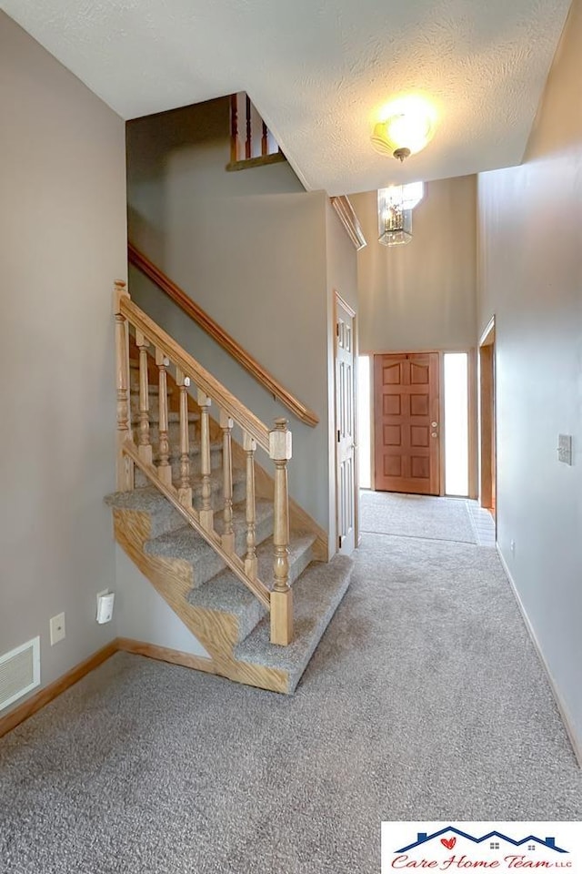 stairway with carpet, a notable chandelier, a textured ceiling, and a high ceiling