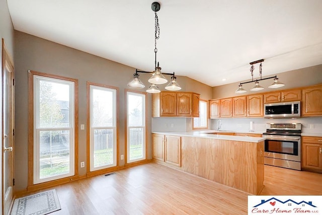 kitchen featuring kitchen peninsula, light wood-type flooring, hanging light fixtures, and appliances with stainless steel finishes