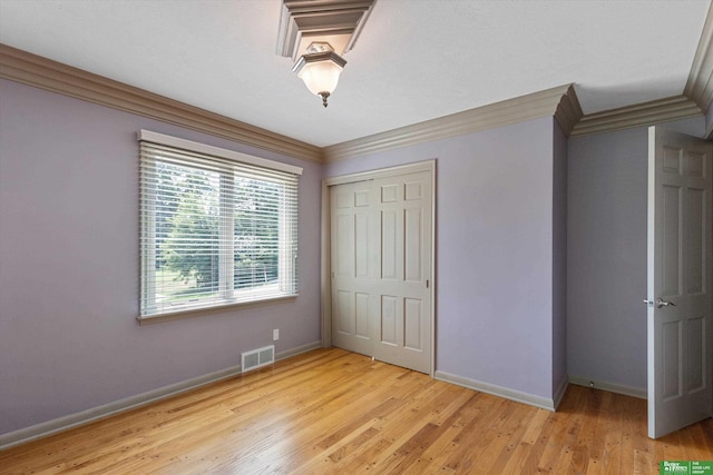 unfurnished bedroom with light wood-type flooring, ornamental molding, and a closet