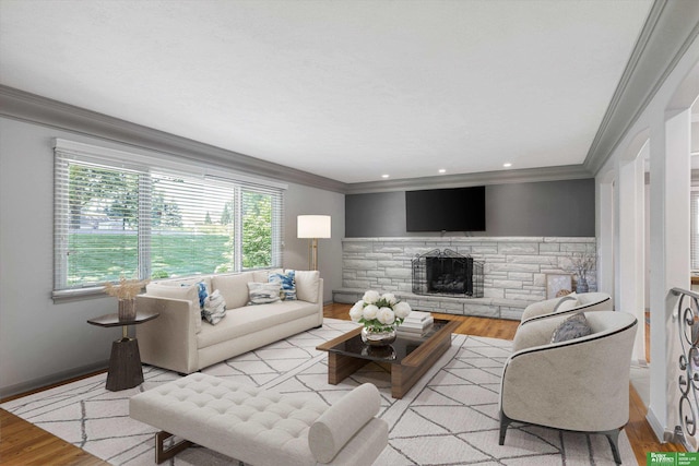 living room featuring a stone fireplace, crown molding, and light wood-type flooring