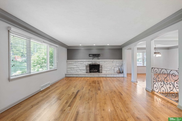 unfurnished living room featuring an inviting chandelier, crown molding, a fireplace, wood-type flooring, and decorative columns