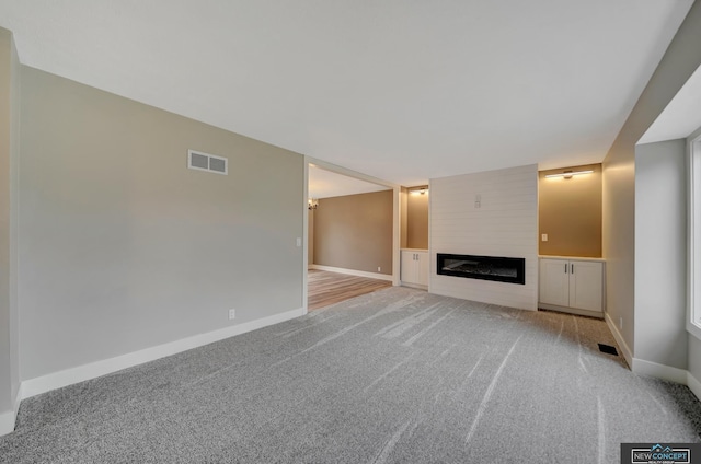 unfurnished living room with a fireplace, built in features, and light colored carpet