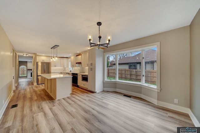 kitchen with stainless steel fridge, decorative light fixtures, white cabinetry, a chandelier, and a kitchen island