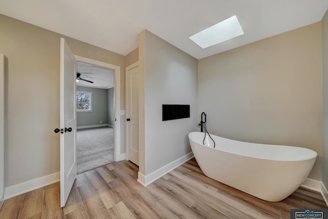 bathroom with a bathing tub, ceiling fan, hardwood / wood-style flooring, and a skylight