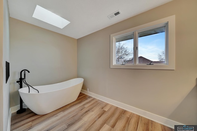 bathroom with a skylight, a bath, and wood-type flooring