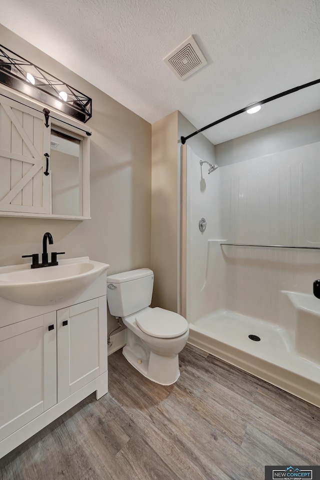 bathroom with a textured ceiling, vanity, a shower, hardwood / wood-style floors, and toilet