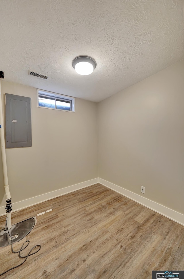 basement featuring wood-type flooring, a textured ceiling, and electric panel