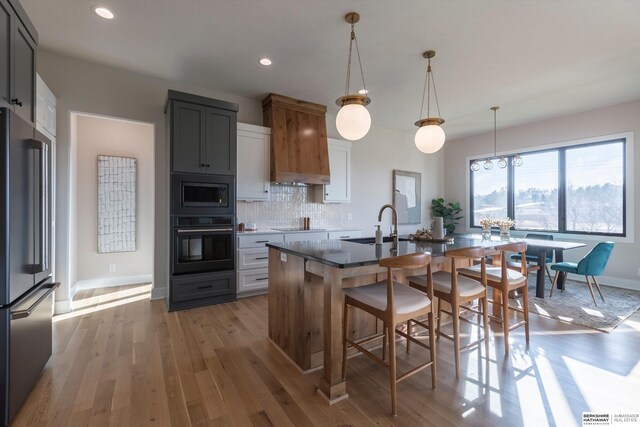 kitchen featuring tasteful backsplash, black appliances, a center island with sink, gray cabinets, and hanging light fixtures