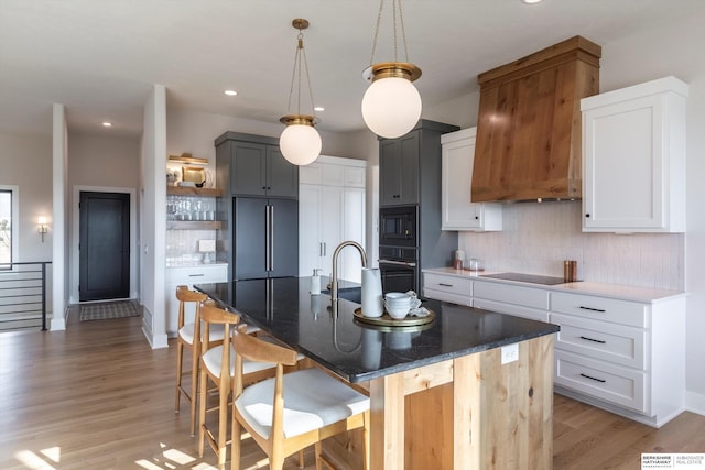 kitchen featuring backsplash, a kitchen island with sink, and white cabinets