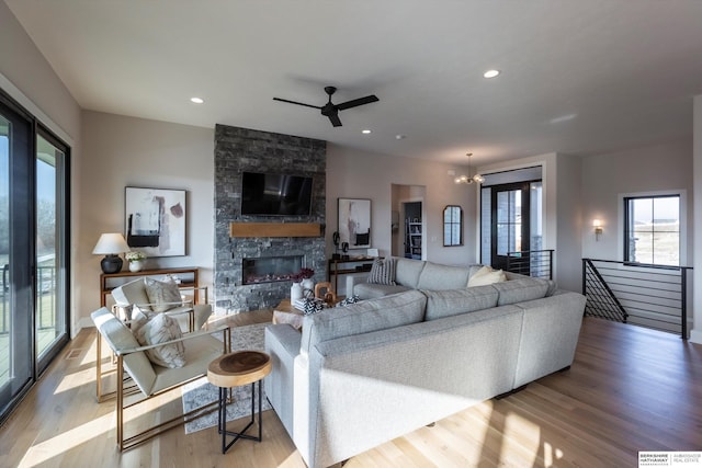 living room with ceiling fan with notable chandelier, light hardwood / wood-style floors, and a stone fireplace