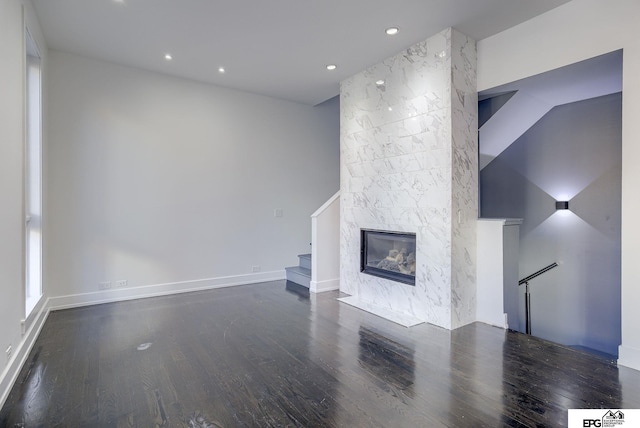 unfurnished living room with a stone fireplace, dark wood-type flooring, and lofted ceiling