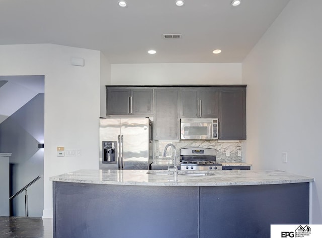 kitchen with sink, light stone counters, backsplash, kitchen peninsula, and appliances with stainless steel finishes