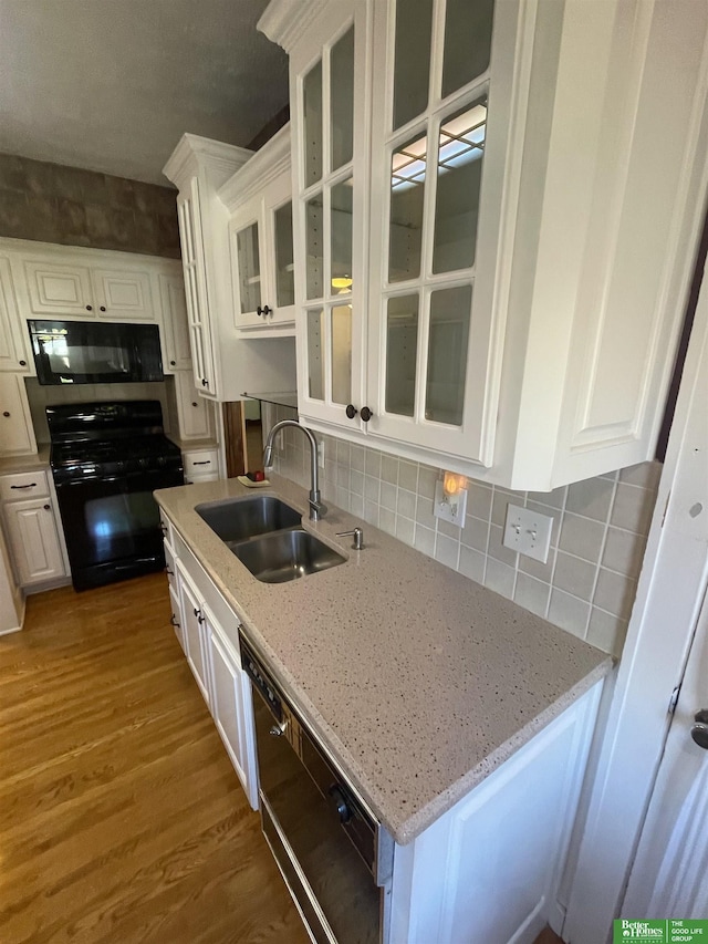 kitchen with light stone countertops, black appliances, white cabinetry, sink, and hardwood / wood-style flooring