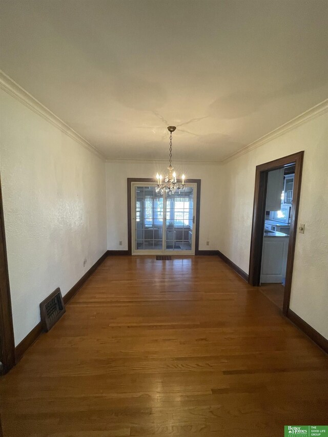 unfurnished dining area featuring dark wood-type flooring, an inviting chandelier, and ornamental molding