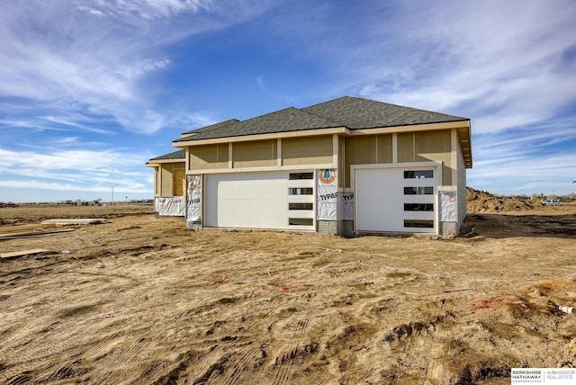 exterior space featuring stucco siding, an attached garage, and roof with shingles