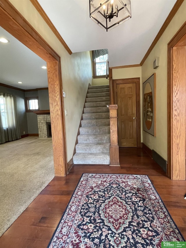 staircase featuring a fireplace, an inviting chandelier, wood-type flooring, and ornamental molding