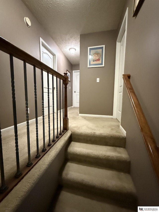 staircase with a textured ceiling, carpet flooring, and baseboards