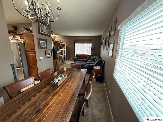 carpeted dining area featuring a textured ceiling, baseboards, and a notable chandelier