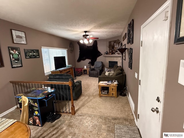 living room featuring a textured ceiling, a fireplace, a ceiling fan, baseboards, and carpet