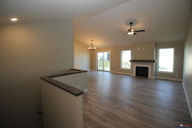 unfurnished living room with ceiling fan with notable chandelier, dark wood-type flooring, and vaulted ceiling