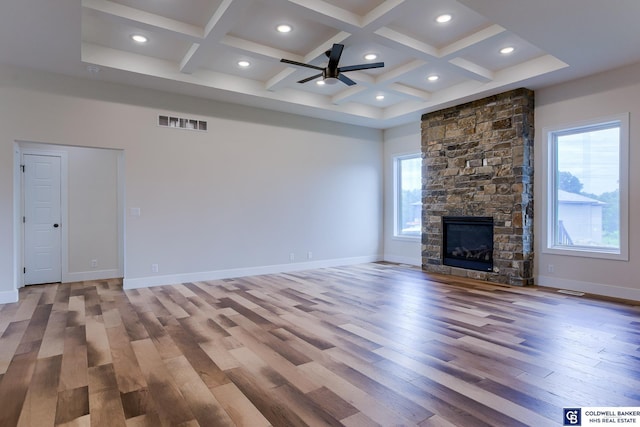 unfurnished living room featuring beam ceiling, ceiling fan, coffered ceiling, a stone fireplace, and wood-type flooring