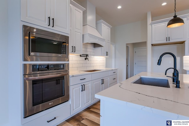 kitchen featuring stainless steel microwave, sink, tasteful backsplash, white cabinets, and custom range hood